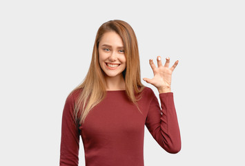 Portrait of cute girl, showing teeth like while roaring, raising hand like paw while pretending lioness, looking flirtatiously at camera. Beautiful young woman isolated on white background in Studio