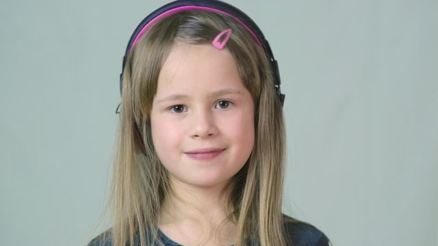 Pretty smiling cild girl listening to music in big pink earphones.