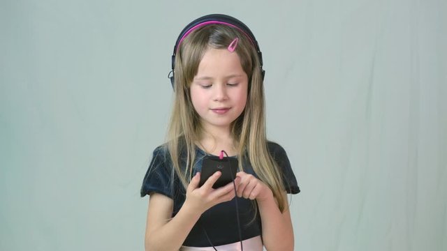 Pretty smiling cild girl listening to music in big pink earphones.