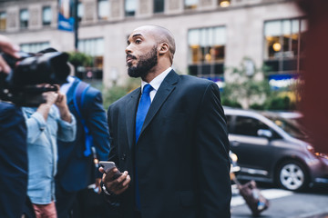 Handsome entrepreneur in suit standing with smartphone