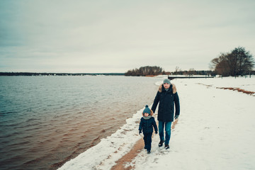 son and father in warm clothes walking together near the lake