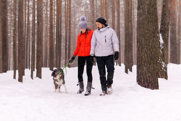 Fototapeta na wymiar young couple walking a dog in the winter forest, the dog wants to play