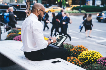 Ethnic man using tablet on street bench