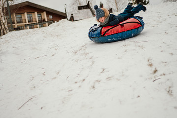 Fototapeta na wymiar male child sledding on the tubing bun, having fun in winter