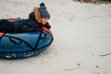 Fototapeta na wymiar side view of small boy having fun on inflatable snow tube sledding in witer park