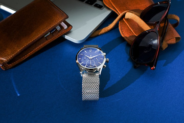 Leather purse, watch with a metal bracelet, sunglasses and laptop on blue background. Accessories for men. Top view