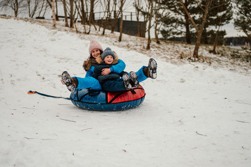 happy son and his mother sledding on the inflatable snow tube down the hill together