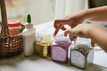 Child's hands taking up containers of glitter for making art work
