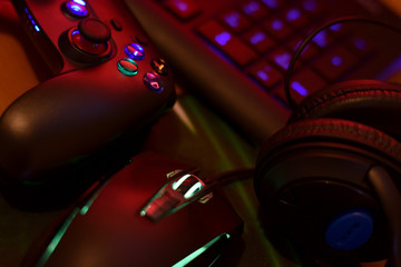 Modern gamepad and gaming mouse lies with keyboard and headphones on table in dark playroom scene. Computer game competition concept