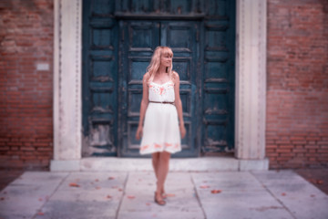 Fototapeta na wymiar Blonde woman in white dress stands alone on stony antic street.