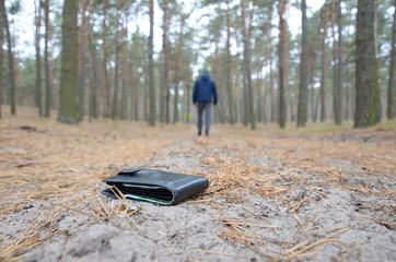 Young man loses his purse with euro money bills on Russian autumn fir wood path. Carelessness and losing wallet concept