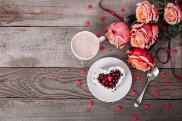 Mini romantic dessert cake for Valentine's Day with roses. Sweet cookies with cream topping and red heart for decor on wooden background. Close-up, copy space.