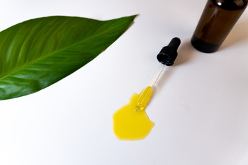 Top view of a bottle with CBD oil or any other essential oil and a green leaf on white background