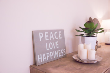 hand-painted motivational wooden vintage board with text Peace, love, happiness.Motivational and inspirational life message about love. Frame and plant with candles on beige background.interior