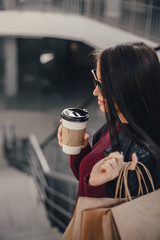 Young pretty woman blogger with smartphone, cup of coffee and shopping bags in city mall