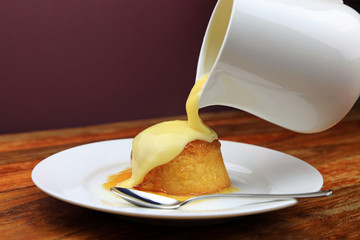 Hot custard being poured from a jug over a treacle sponge pudding. - obrazy, fototapety, plakaty