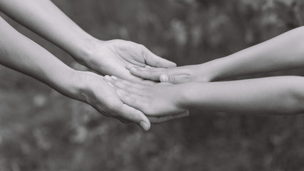 Closeup view of mother and little child holding hands together. Horizontal black and white color photography.