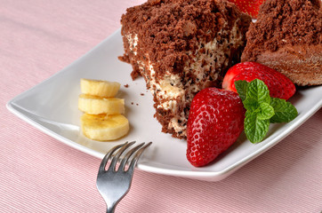Homemade mole hole cake with whipped cream, banana, strawberries and fresh mint leaves on white decorative shaped plate. Pink place setting. Close-up.