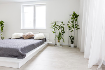 Light bedroom with white wall, large bed with grey bedding and handmade furniture