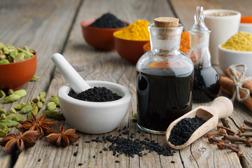 Black cumin or roman coriander seeds, black caraway oil bottles and aromatic spices and herbs: turmeric, cardamom, cinnamon, cloves, anise, paprika.