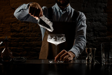 Professional male bartender putting a crushed ice to the big cocktail glass with special spoon