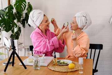 Mother and daughter in bathrobes and towels on head using natural cosmetics and having fun together...