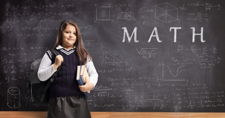 Female pupil in a school uniform standing in front of a chalkboard with math