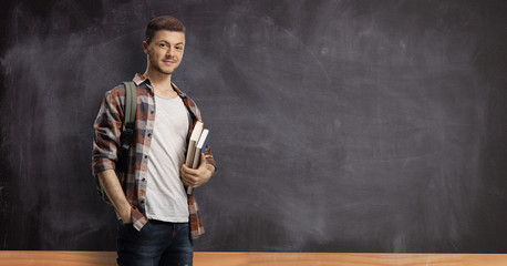 Male student in front of a blackboard holding books