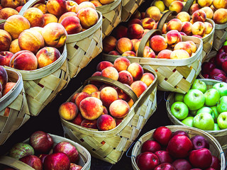 An assorted variety of baskets of fruits including apples and peaches