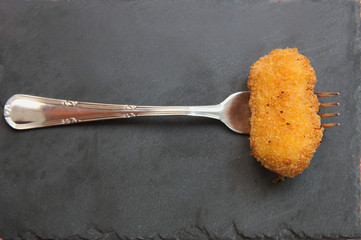 A homemade croquette on a fork on a black slate plate