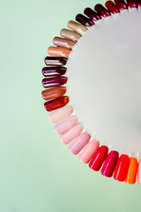 Obraz premium Nail polish in different fashion color. Colorful cats eye 3D nail lacquer in tips and mock-up blank bottle isolated on pastel background.healthy nails.Selective focus. Copy space.Finger nail art