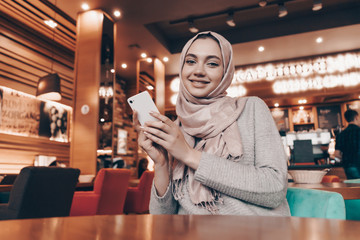 Muslim woman in a cafe with a phone in her hands sitting at a table