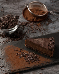 Raw chocolate cheesecake on dark grey background. Healthy organic dessert pie. Cacao and chocolate around