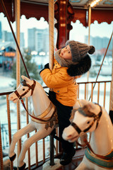 boy having fun riding carousel horse and looking at the camera at daytime