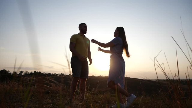 Young beautiful girl runs up to her boyfriend and hugs him. Happy couple kisses against the backdrop of the bright sunset in the evening, slow motion. The guy circles the girl. Unusual romantic date.