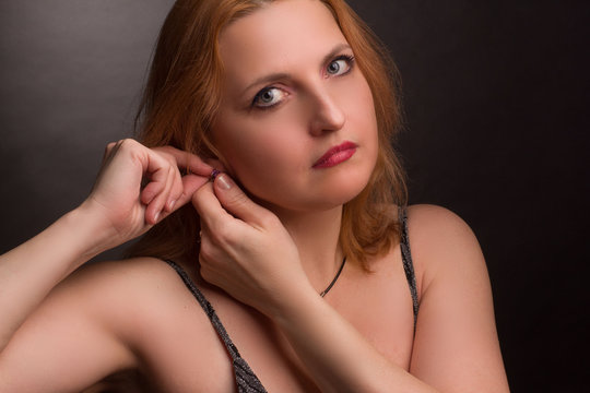 portrait of a blonde plus-size model in a dark dress with straps on a dark background in the Studio