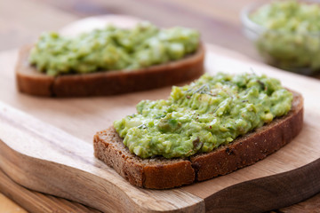 Healthy food. Rye bread with guakomole, avocado pasta on wooden cutting board. Avocado toast for breakfast.