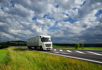White truck driving on the asphalt road in a rural landscape