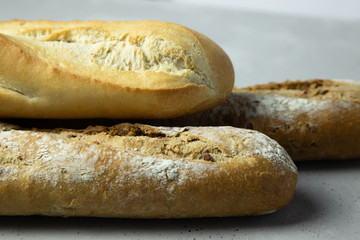 Close-up of three whole grain baguettes and one made from wheat flour, one on top of the other. Gray background.
