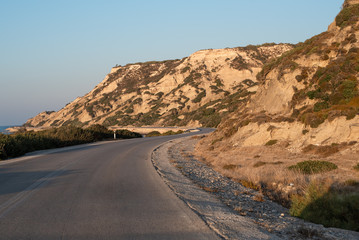 The road between mountains and sea. Sunset in Greece and lonely winding road.
