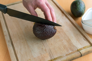 Frauenhand hält Avocado um sie mit dem Messer in zwei hälften zu schneiden