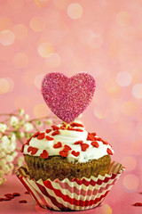 Delicious cupcake for Valentines Day close-up. Cupcake with white cream and a red heart on a pink background, bokeh effect, vertical layout, copy space
