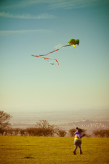 Boy playing outside with a kite, running outdoors during the day with retro style filter