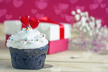 Saint Valentine's Day card. Cupcake with white cream and red hearts and a box with a gift on a pink background, bokeh effect, copy space