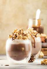 Cold chocolate dessert with whipped cream, popcorn and caramel topping in glasses on beige background, place for text