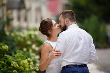 Fototapeta premium Young Bride and Groom couple in summer old City garden. Tender holding each other. woman and man couple. Romantic walk of young happy family near hydrangea bush. lovers newlyweds street style wedding