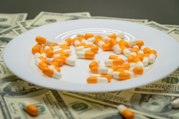 white plate with orange-and-white tablets on the table with dollar bills. Photos of falling tablets in a plate, freezing photos