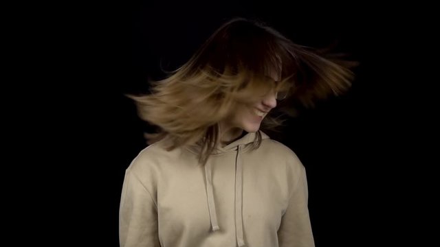 The young woman is actively shaking her head. A woman twirls her head and her hair is shaking on a black background. Slow motion