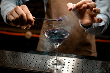 Fototapeta na wymiar Professional bartender decorated purple alcoholic cocktail in a martini glass by a flower with pearl powder