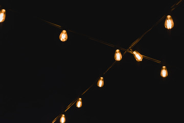 Light bulb decor in outdoor party. Decorative outdoor string lights at night time. Golden glowing garlandon in wedding